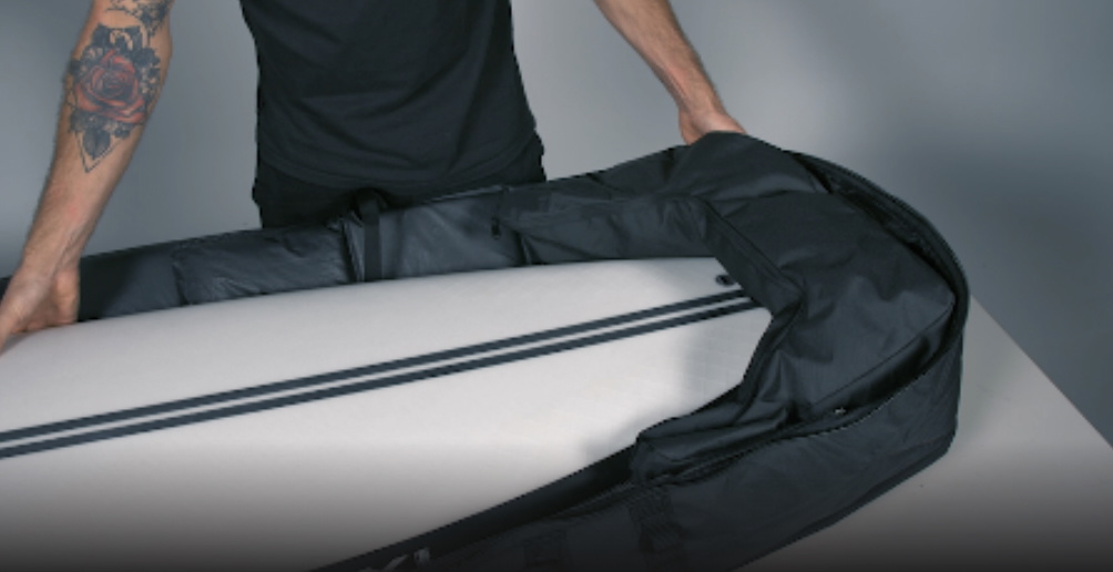 Man sliding a white surfboard into a black padded board bag in a studio
