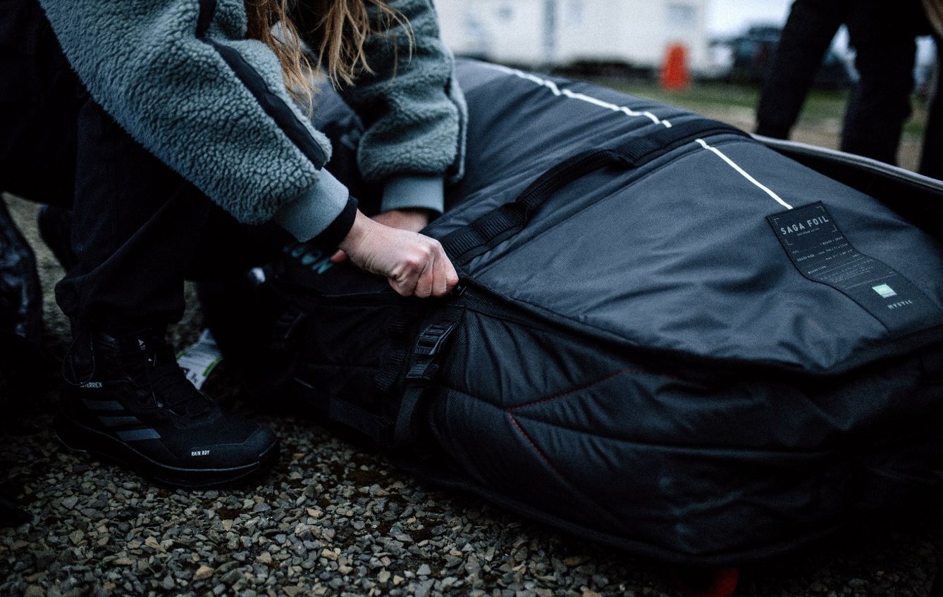 Traveller in a fleece crouching on gravel to zip up a large navy board bag