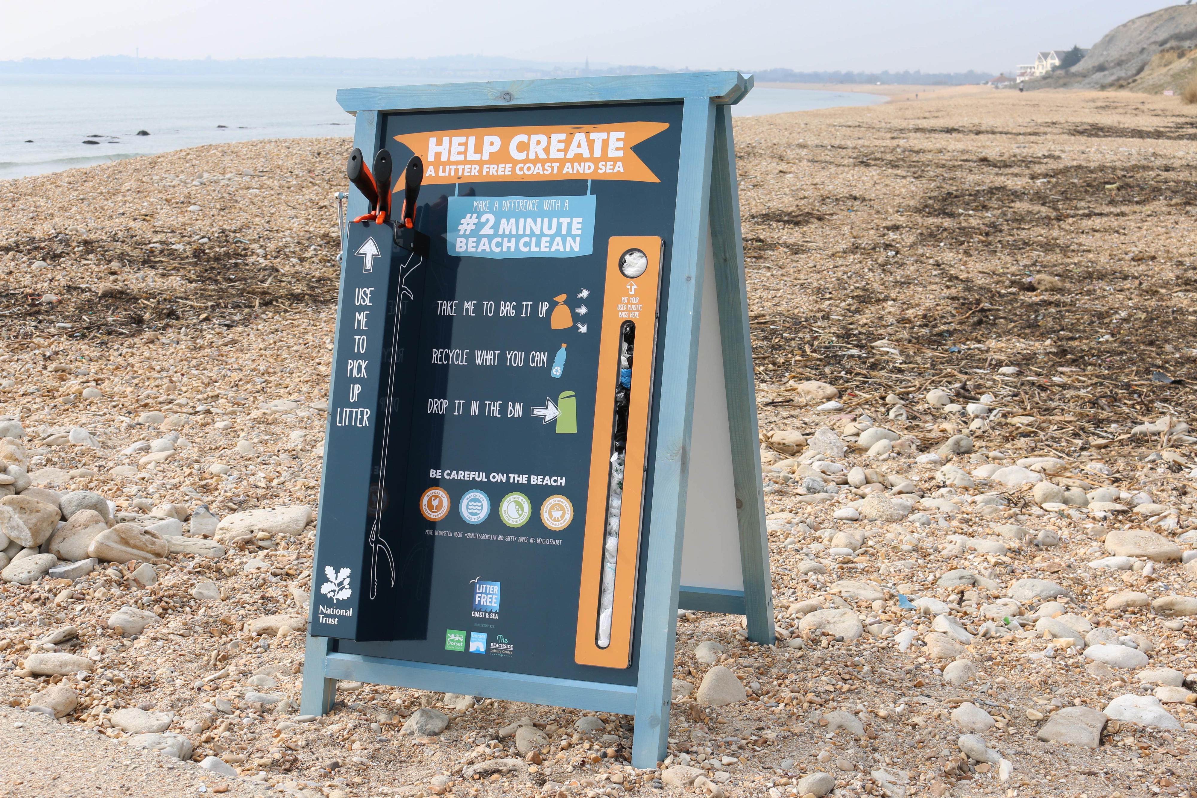 A-board sign on a shingle beach encouraging visitors to do a two minute beach clean
