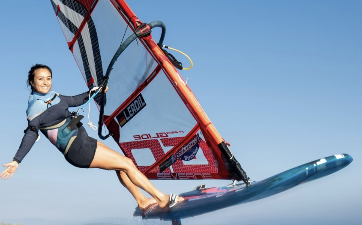 Windsurfer hanging off the boom mid jump against a clear blue sky