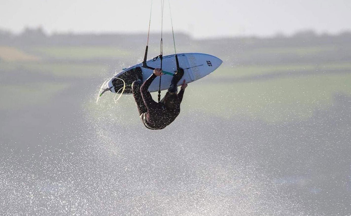 Kitesurfer upside down mid-air in an inverted jump above flat water