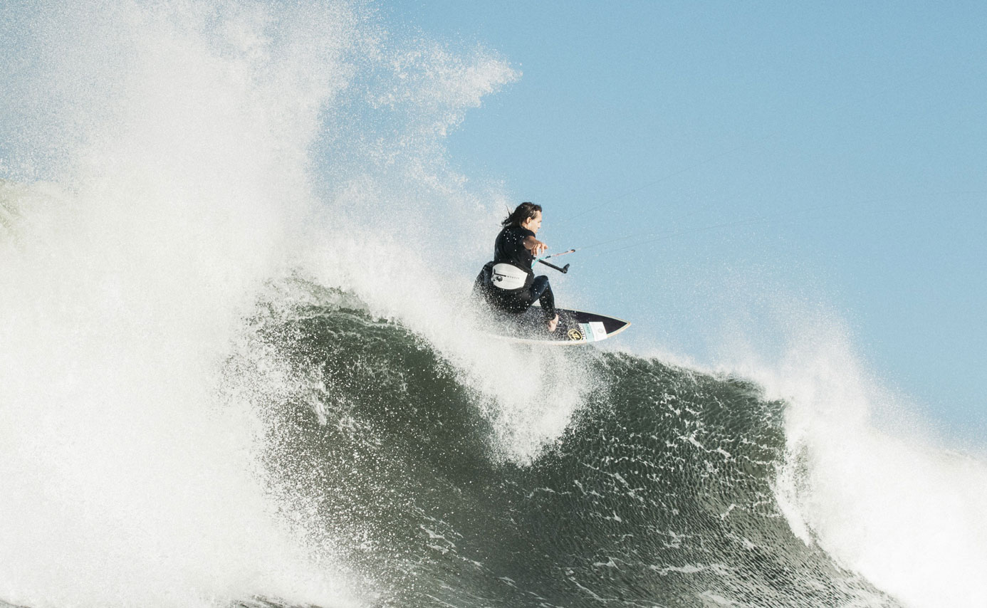 Rider hitting the lip of a large breaking wave, throwing spray into a blue sky