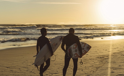Surfisti in muta in controluce davanti a un tramonto